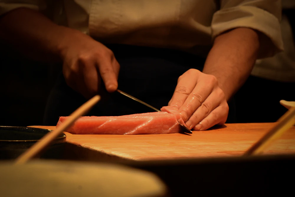 Itamae cortando un lomo de pescado sobre la tabla de la barra