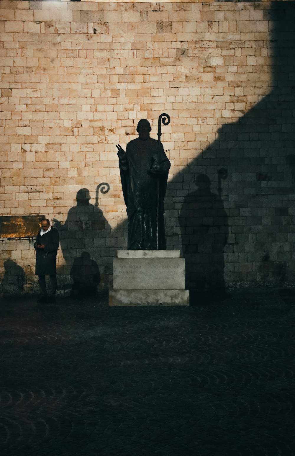 a statue of a man holding an umbrella in front of a brick wall