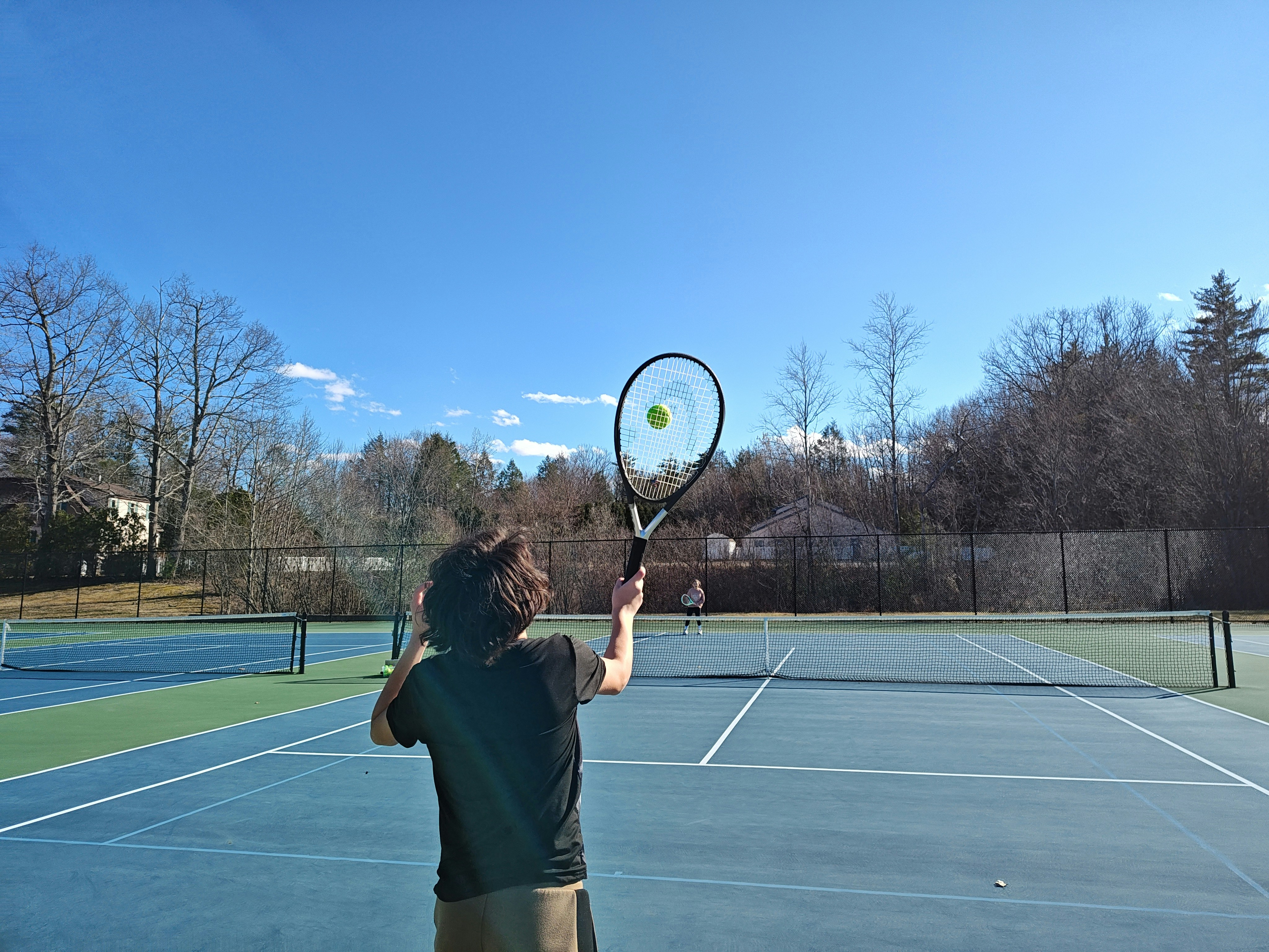 Tennis player serving on a bright blue hardcourt under clear sky in a professional tournament stadium