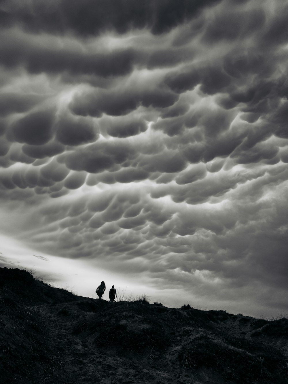 two people standing on top of a hill under a cloudy sky
