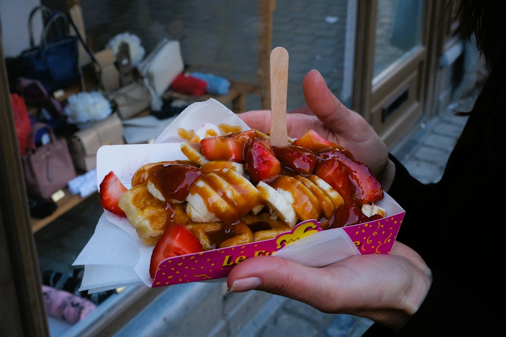 a person holding a box of food with strawberries and bananas