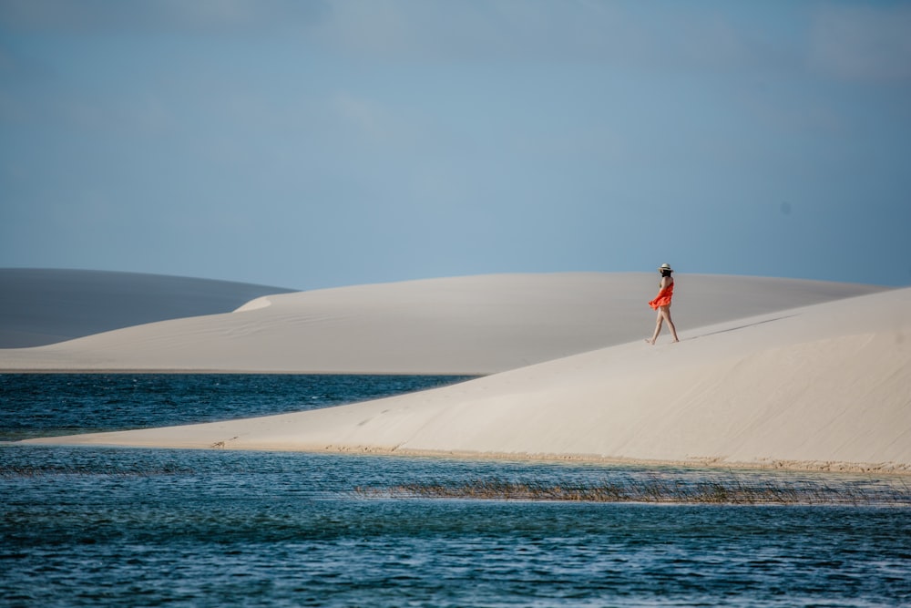 a woman in a red dress standing on top of a sand dune