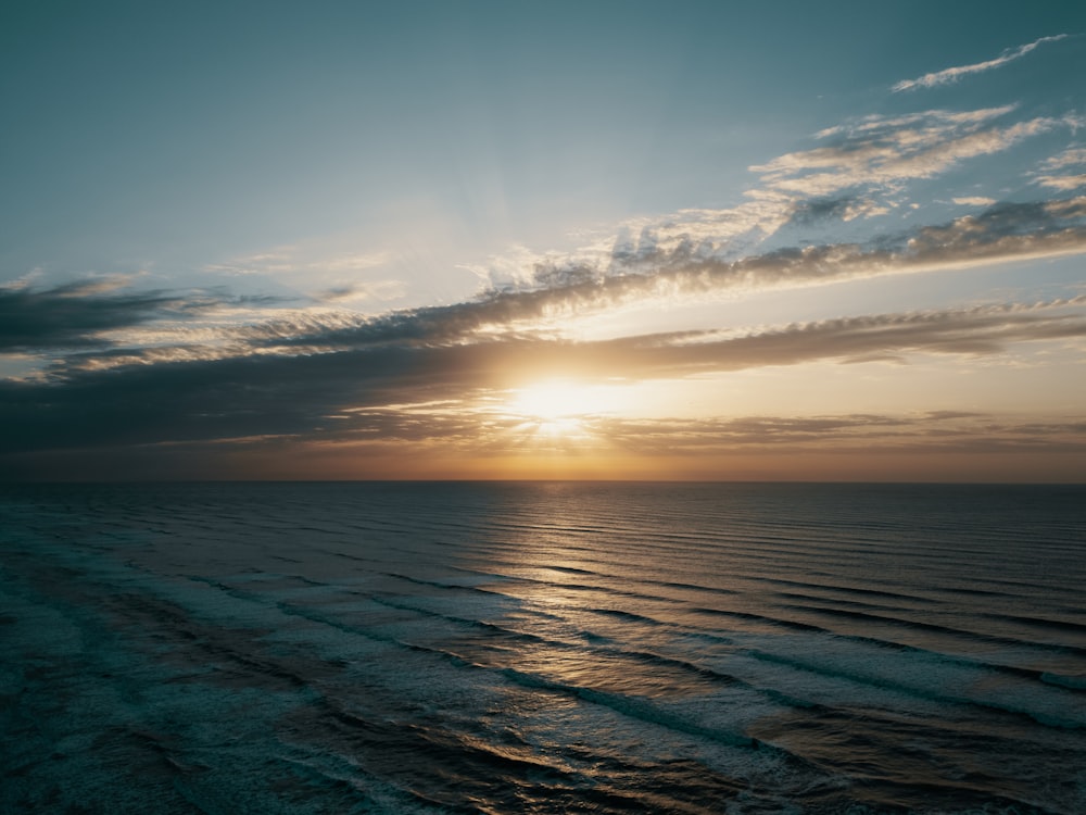 the sun is setting over the ocean on a cloudy day