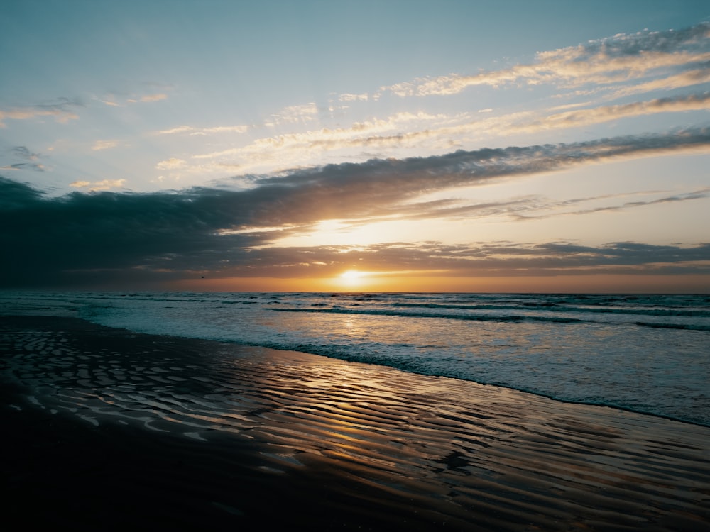 the sun is setting over the ocean on the beach