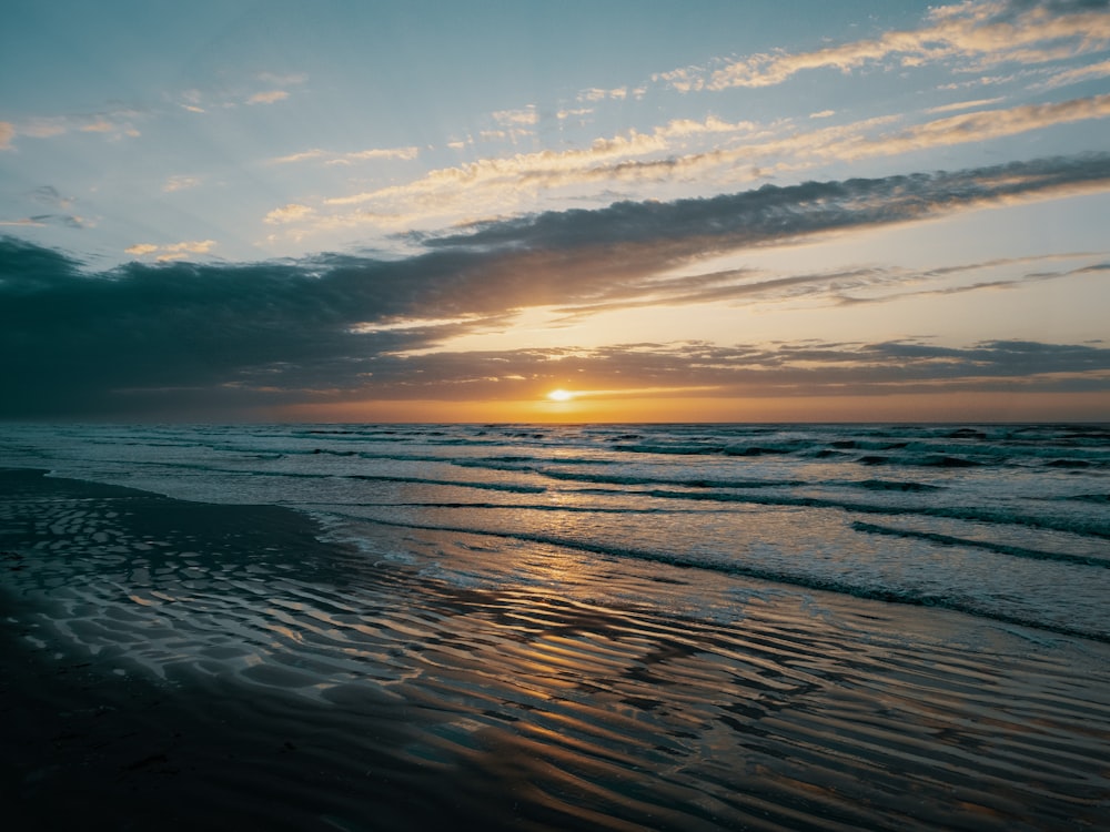 the sun is setting over the water at the beach