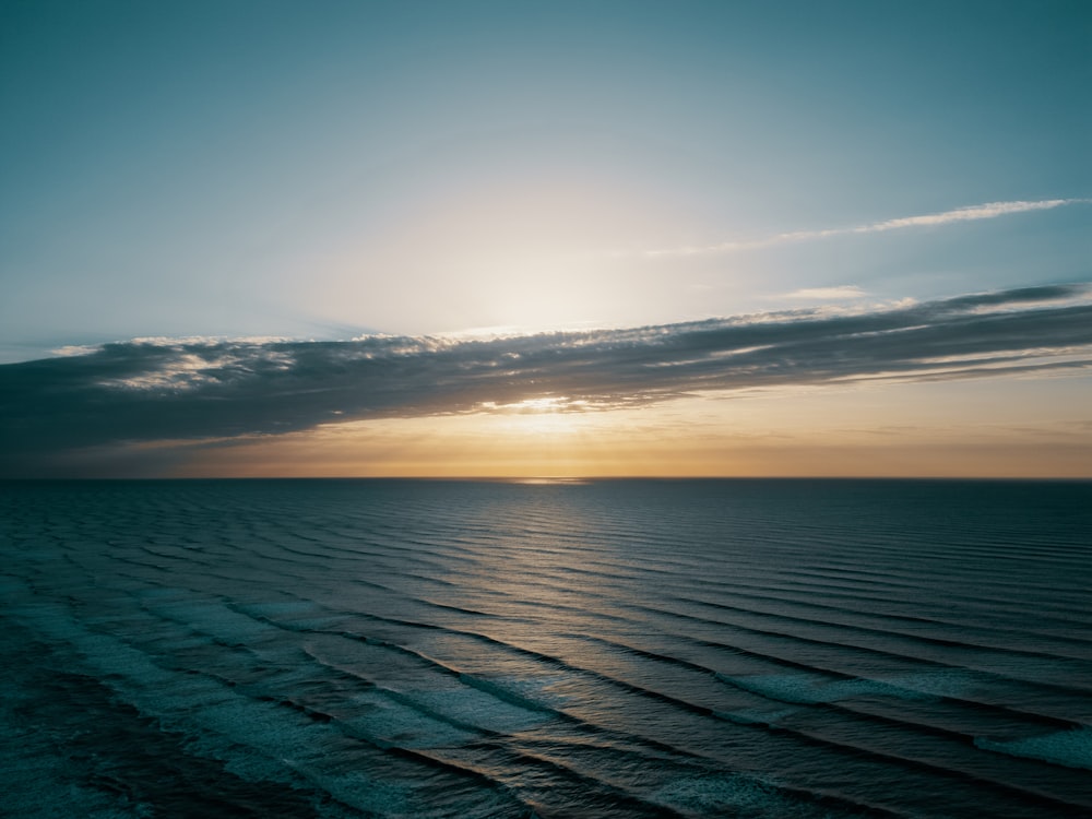 the sun is setting over the ocean on a cloudy day