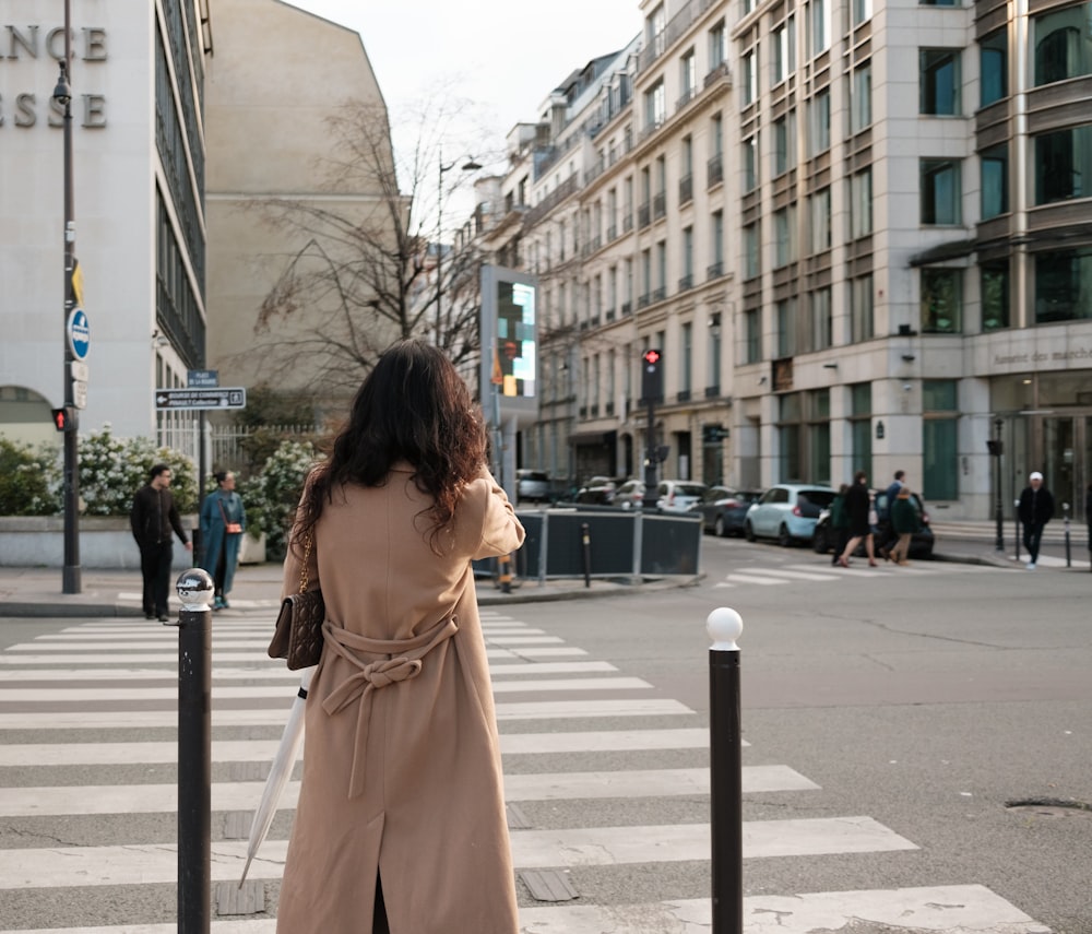 a woman in a trench coat is crossing the street