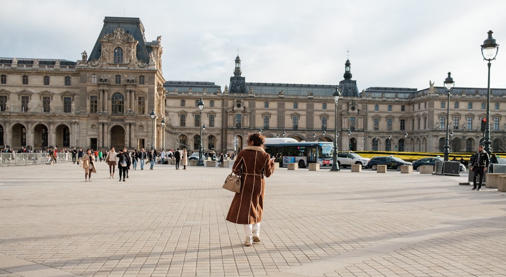 a woman in a brown coat is walking in a courtyard