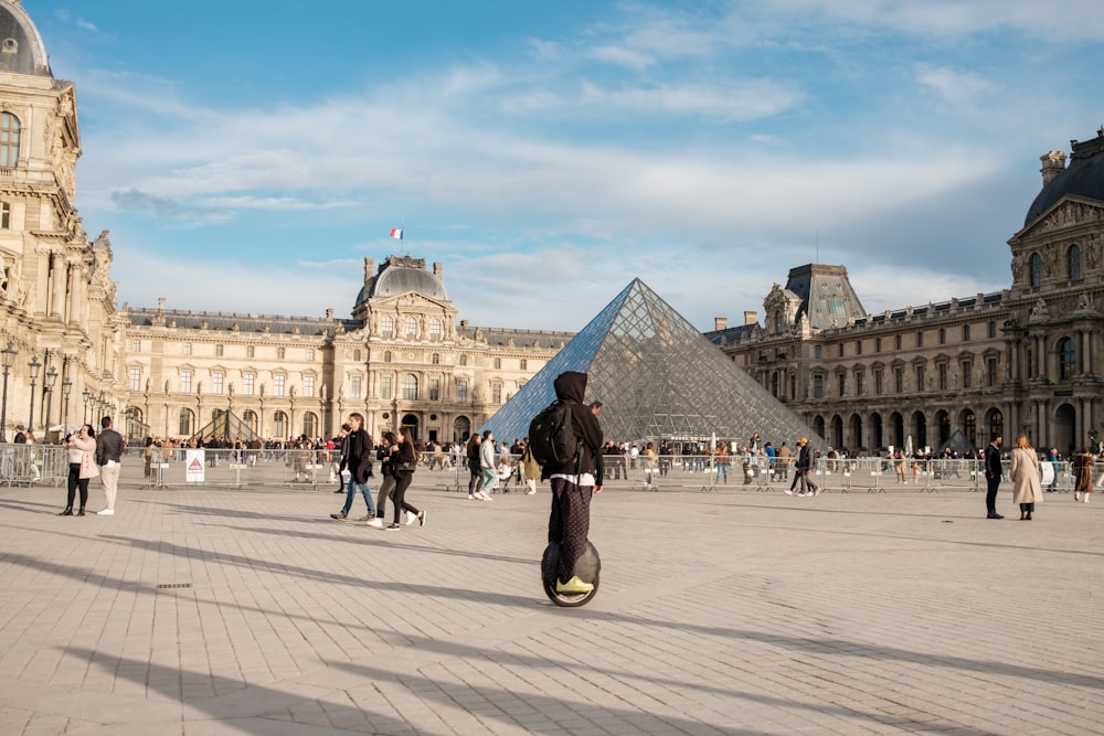 a group of people walking around a courtyard with a pyramid in the background