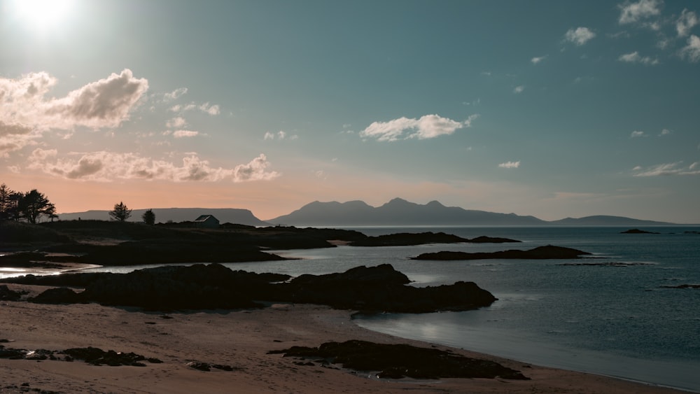 the sun is setting over the ocean with mountains in the background