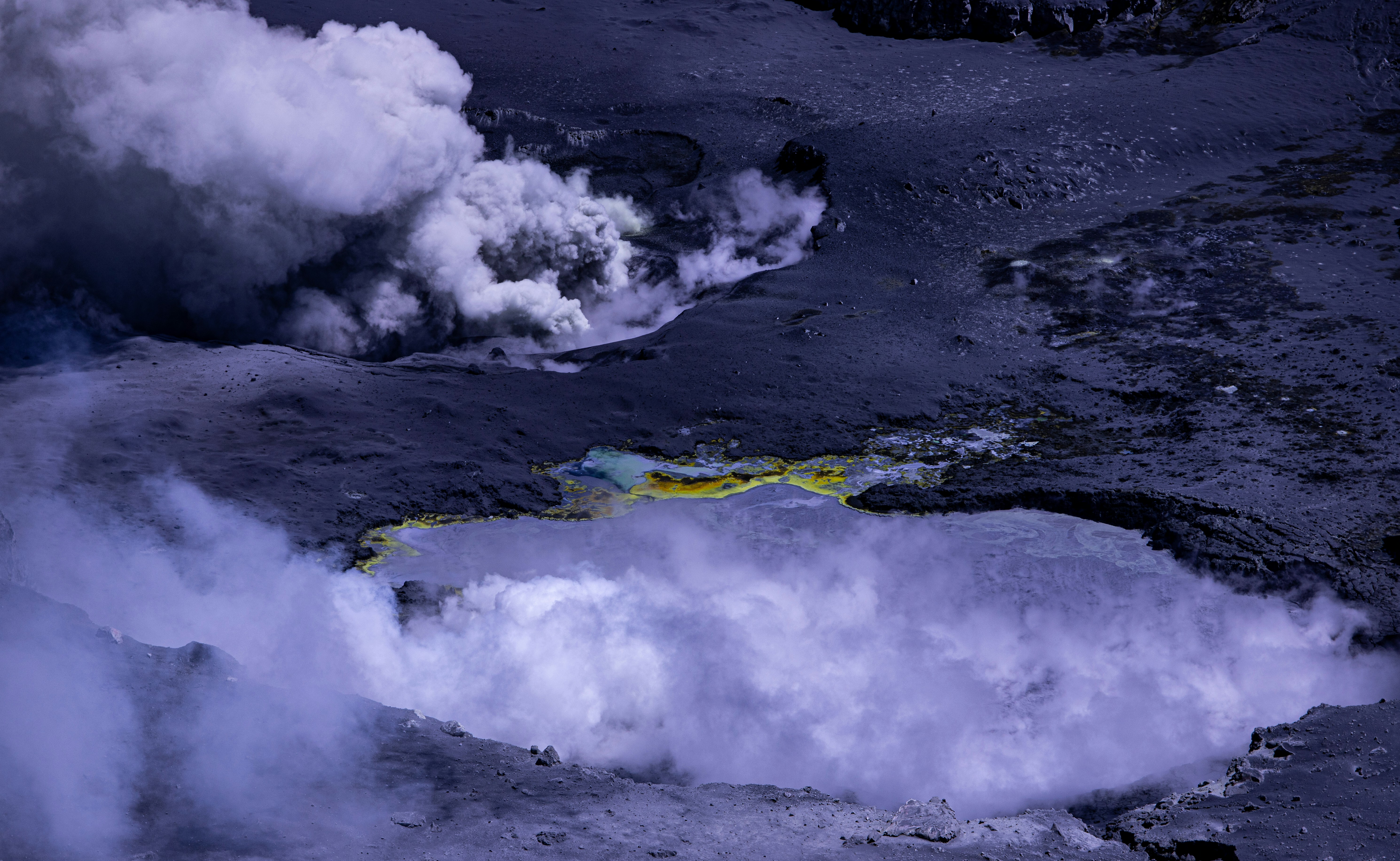 a crater with steam coming out of it, A view of the Poás Volcano, featuring plumes of steam and gases rising from the crater, with sulfur deposits visible around the geothermal areas.