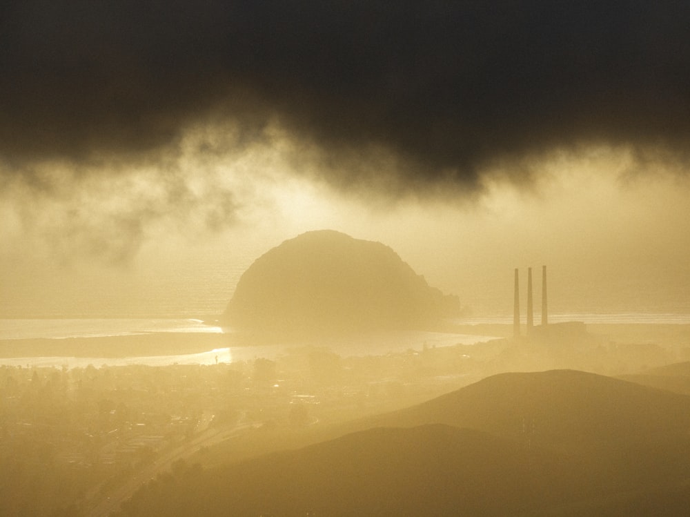 a foggy sky over a city with a large rock in the distance