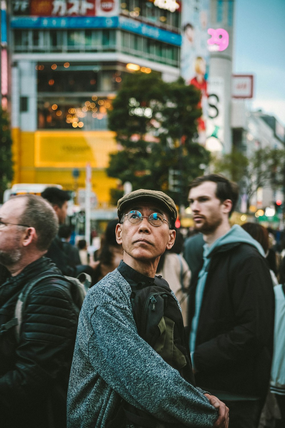 帽子をかぶり、眼鏡をかけた男が大勢の人々の前に立つ