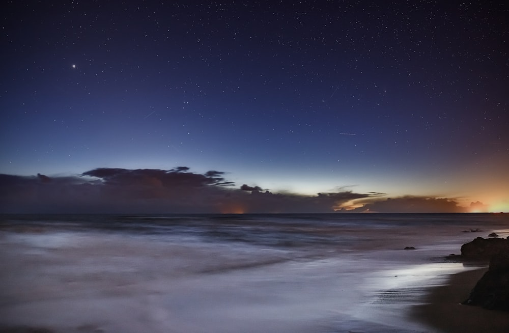 a night sky with stars and clouds over the ocean