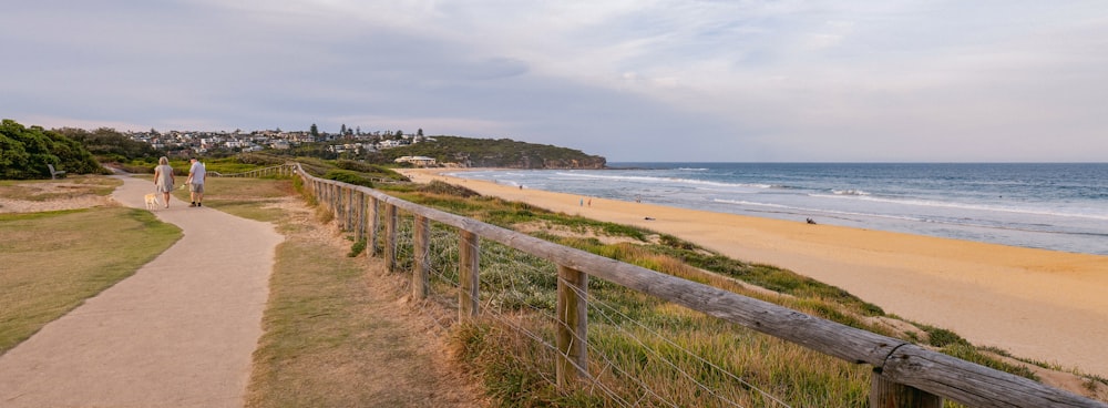 a couple of people walking down a path next to a beach