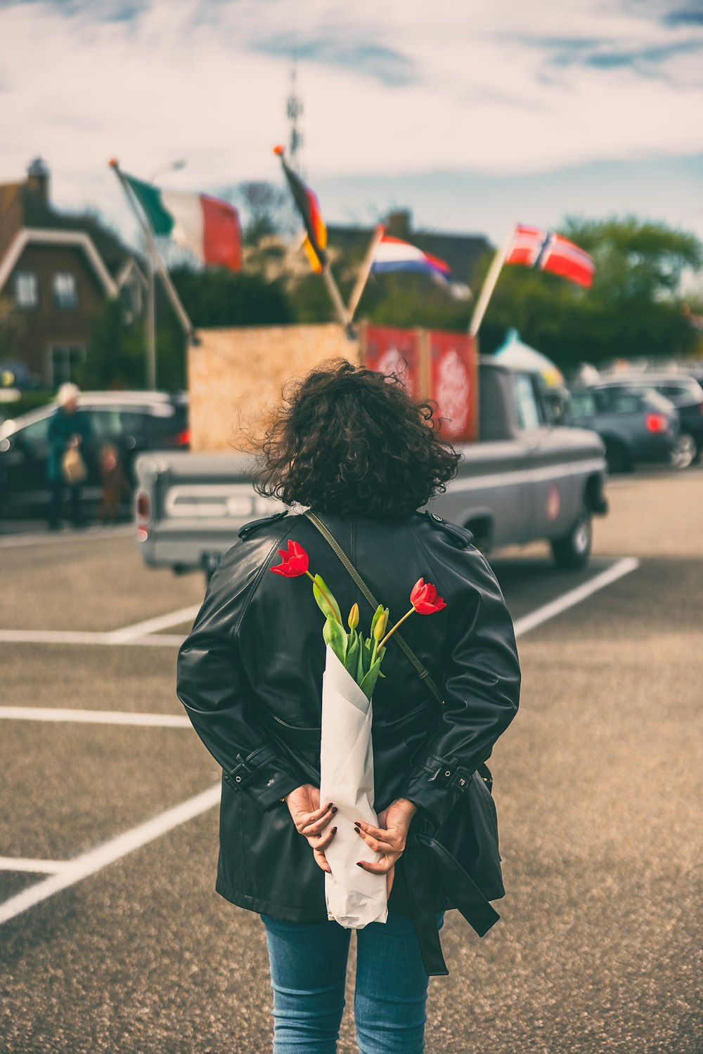 a woman standing in a parking lot holding a bouquet of flowers