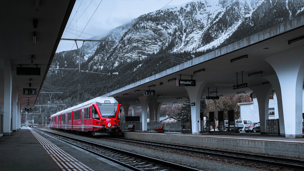 a red train traveling down train tracks next to a snow covered mountain