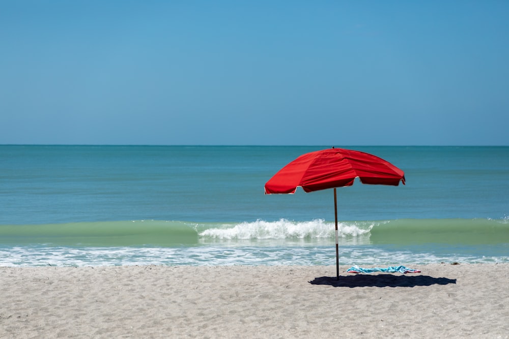 a red umbrella sitting on top of a sandy beach