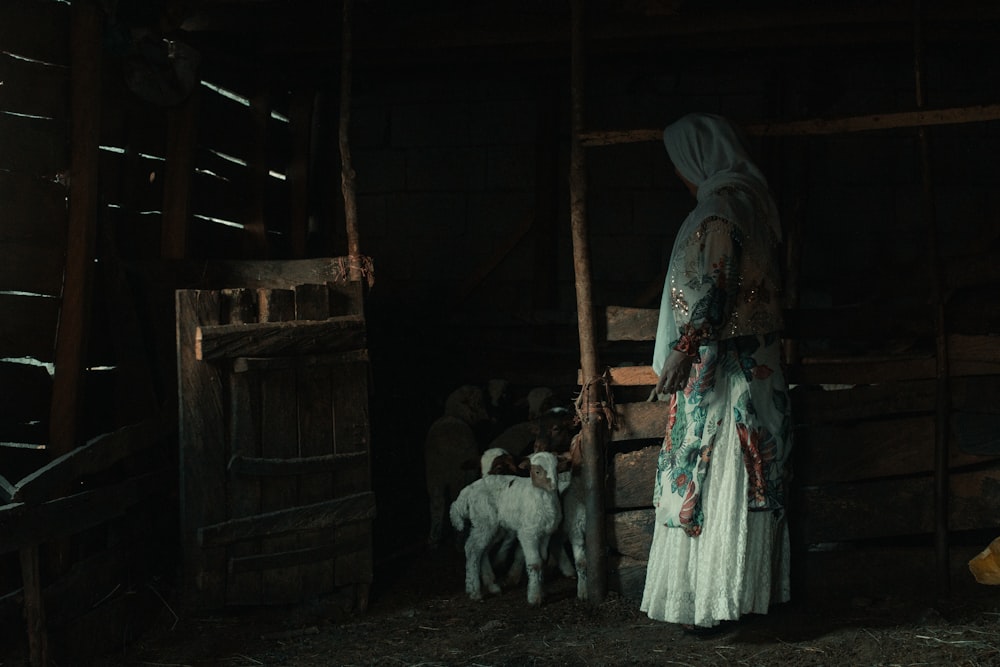 a woman standing in a barn with a lamb