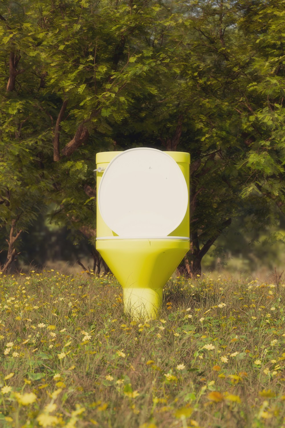 a yellow toilet sitting in the middle of a field