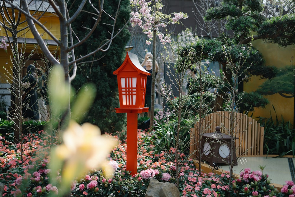 a red birdhouse in a garden with pink flowers