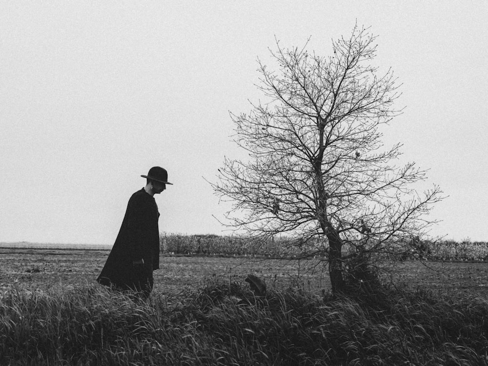 a man standing in a field next to a tree