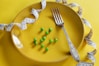 a plate with a fork, measuring tape and green peas