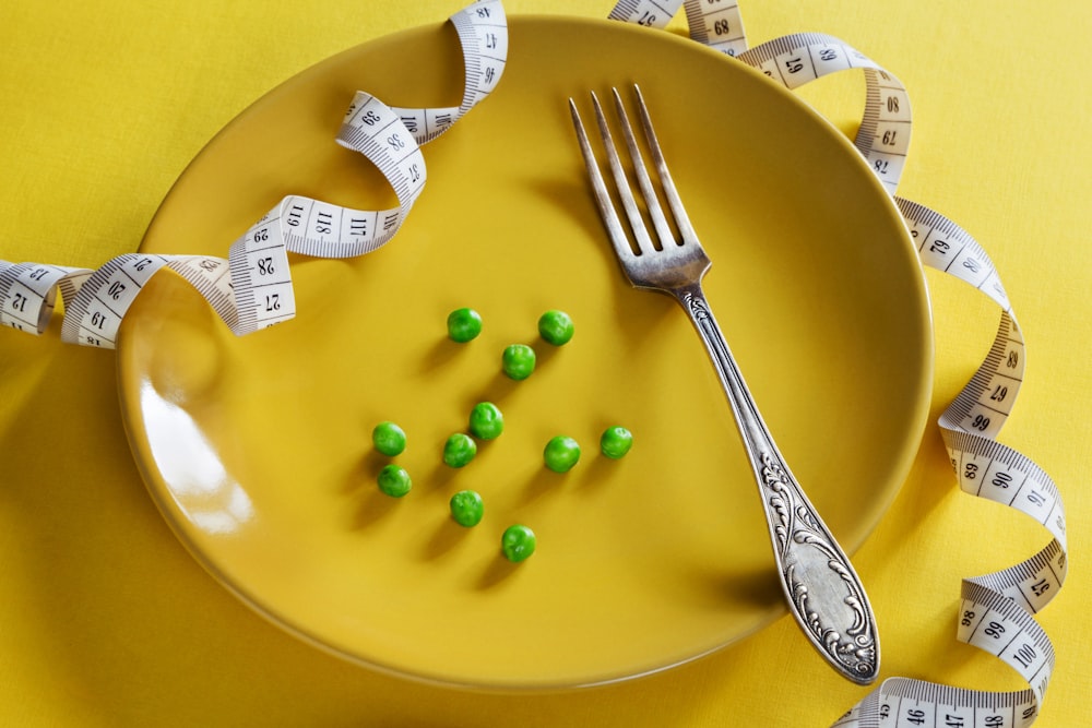 a plate with a fork, measuring tape and green peas