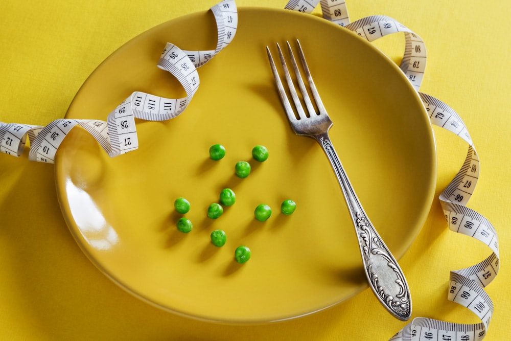 un plato con tenedor, cinta métrica y guisantes