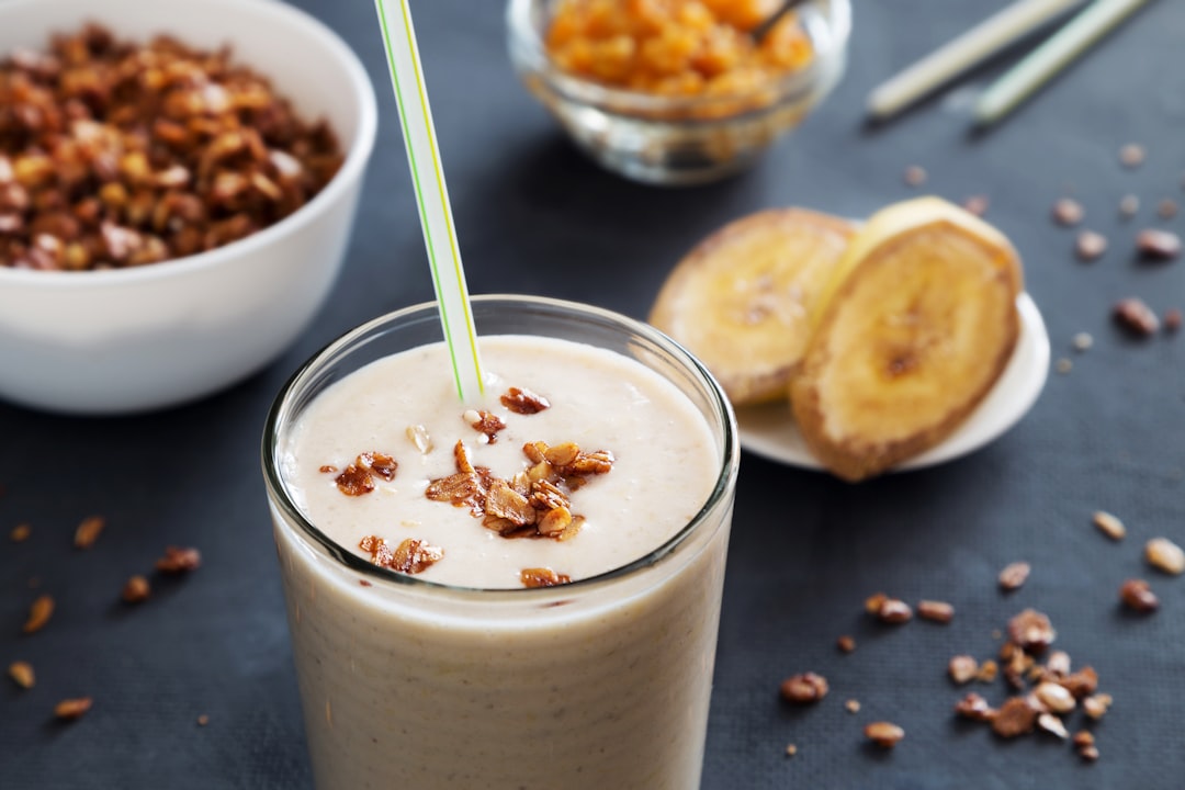 a smoothie in a glass with a straw, Banana milkshake with straw and granola
