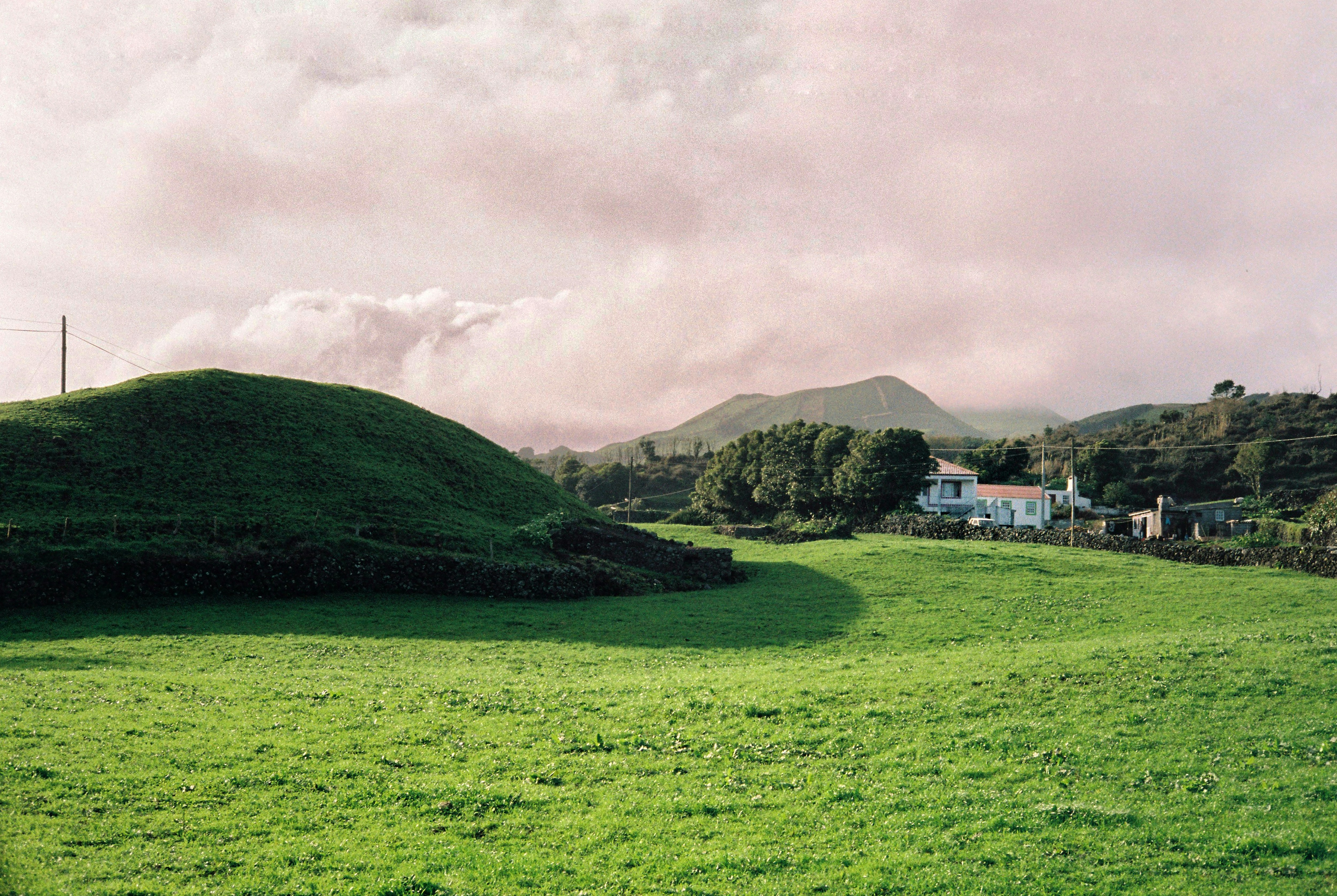 a lush green field with a house in the distance, Grey clouds on Pico Island, Azores on film.