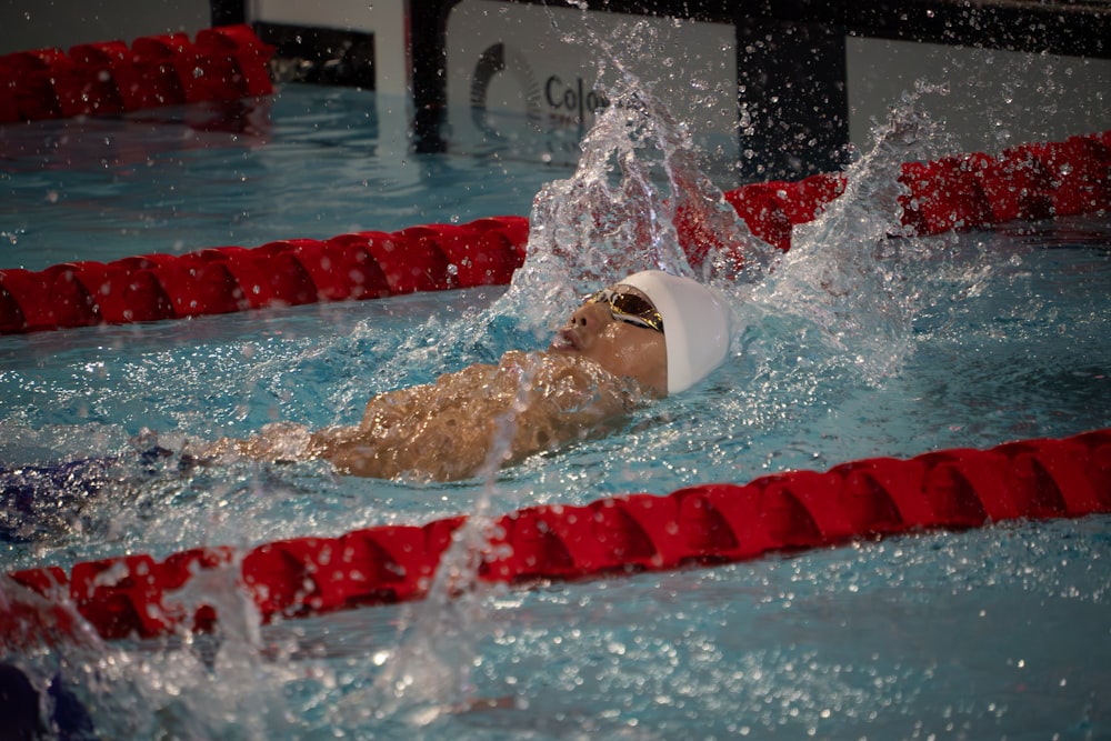 a man swimming in a pool wearing a white hat