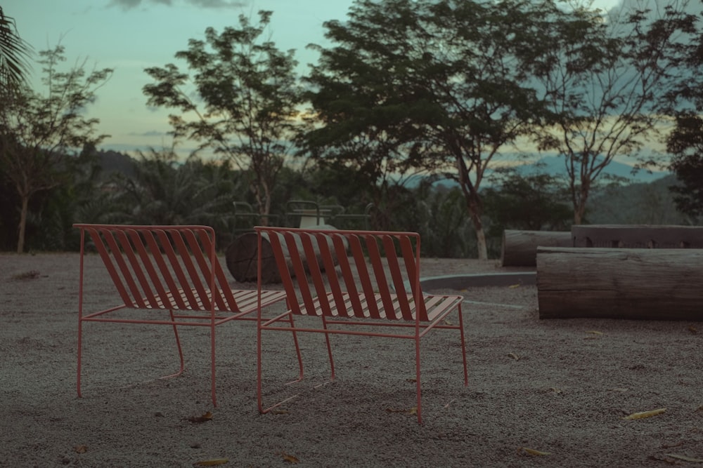 a couple of red chairs sitting on top of a sandy ground