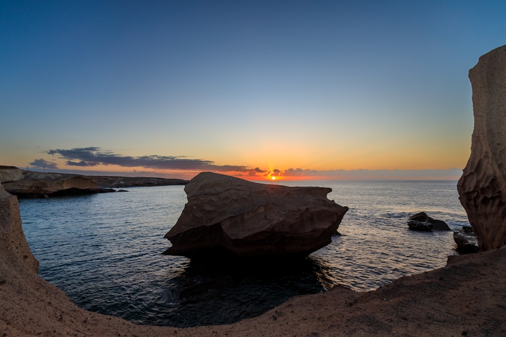 the sun is setting over the ocean with rocks in the foreground