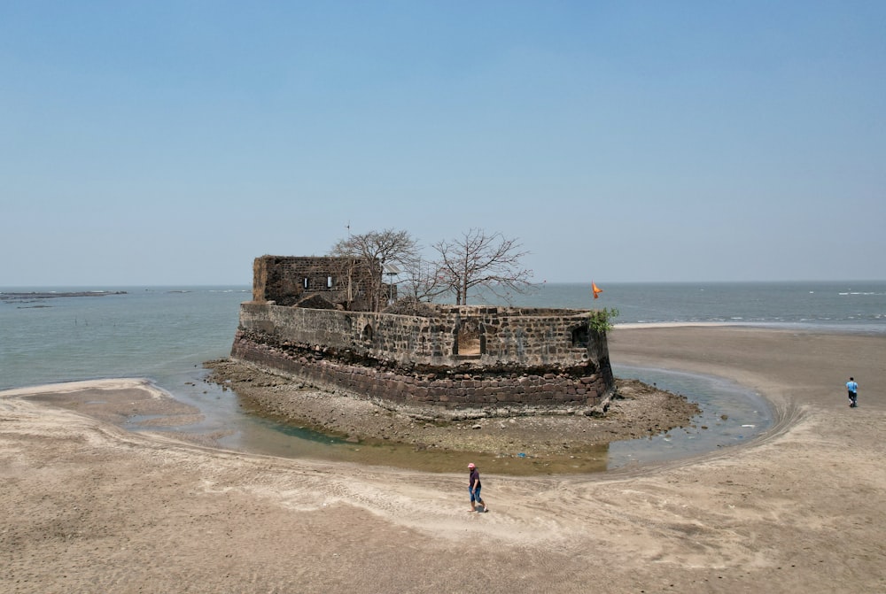 two people walking on a beach next to a castle