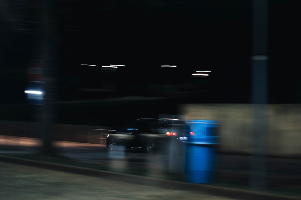 a blurry photo of a car driving past a blue trash can