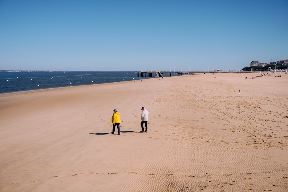 a couple of people standing on top of a sandy beach