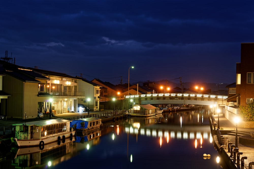 a night scene of a canal with a bridge in the background