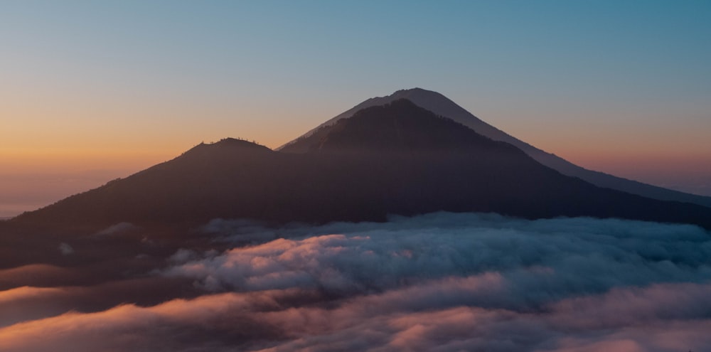 a mountain covered in clouds with a sunset in the background