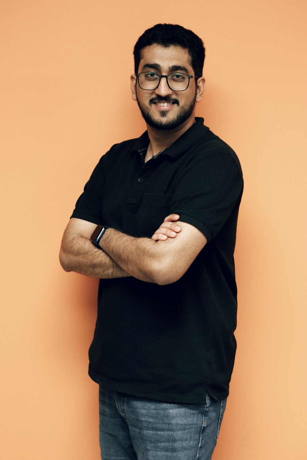 a man standing with his arms crossed in front of an orange wall