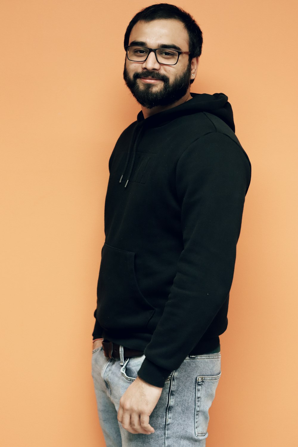 a man with a beard and glasses standing in front of an orange wall