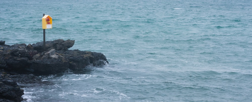 a yellow and white sign sitting on top of a rock near the ocean