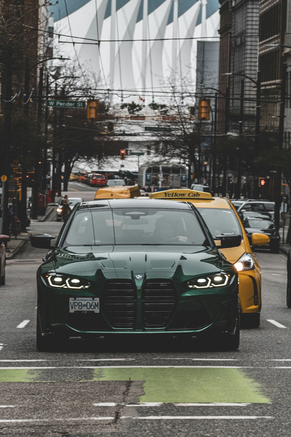 a green car driving down a street next to a yellow taxi