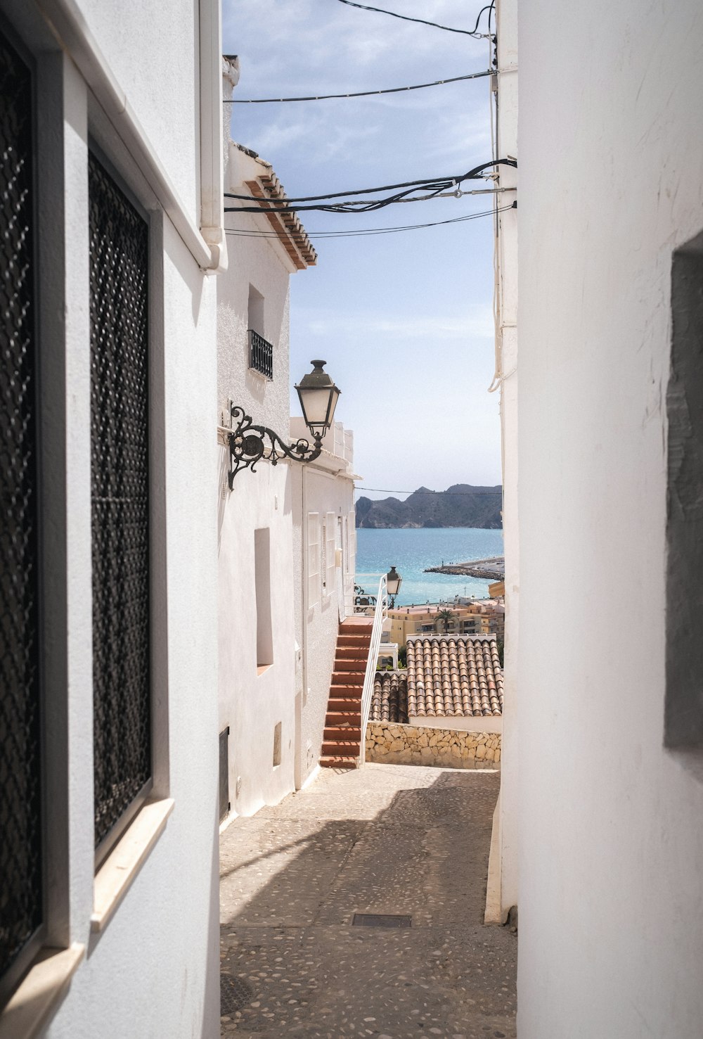 a narrow alley leading to a white building with a blue ocean in the background