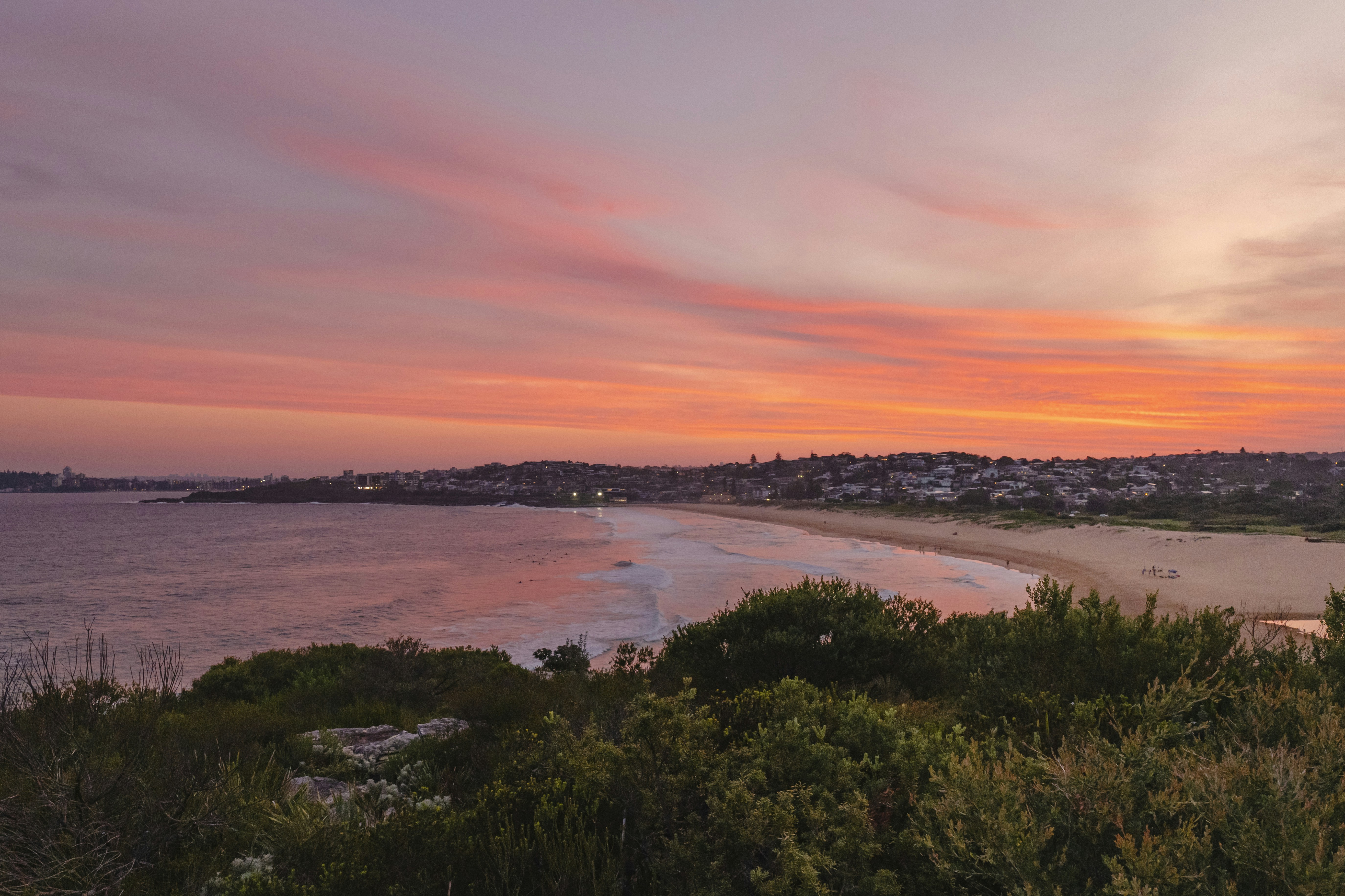 Una vista al atardecer de una playa con una ciudad en la distancia