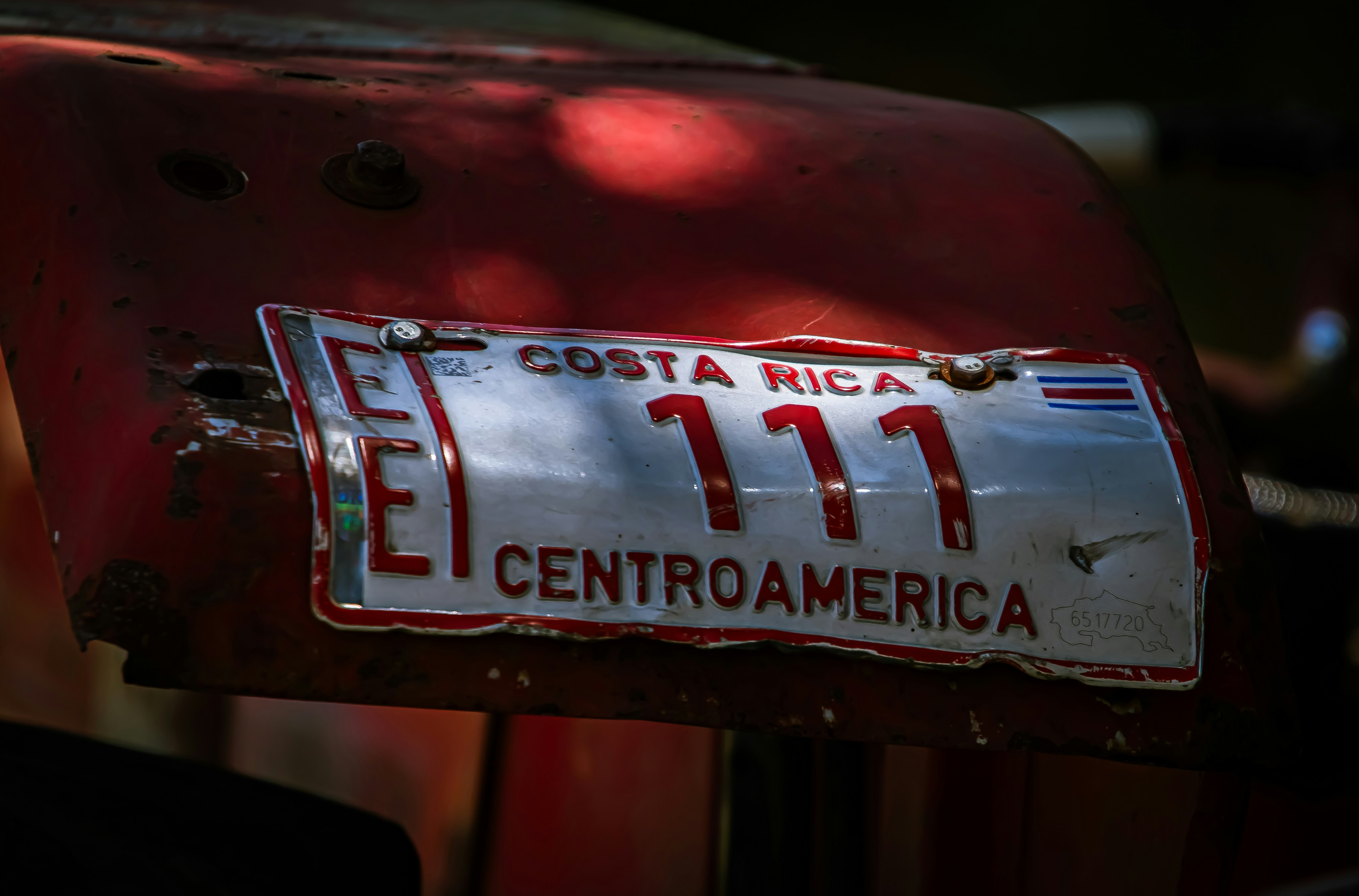 A close-up of a Costa Rican license plate mounted on a red tractor, showing signs of wear and authenticating the vehicle's registration for road use.