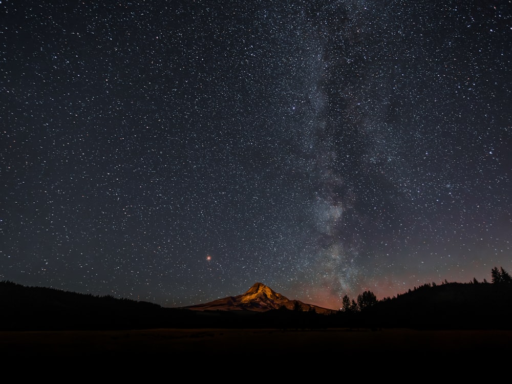 the night sky with stars above a mountain