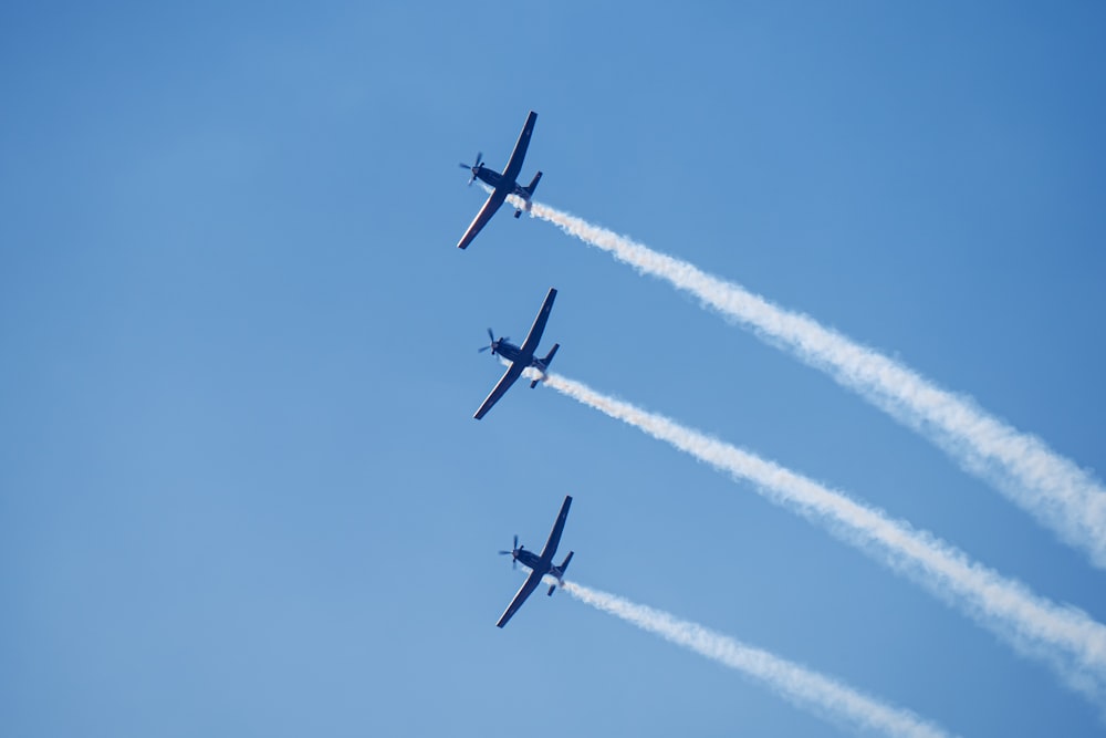 three airplanes flying in the sky leaving a trail of smoke behind them