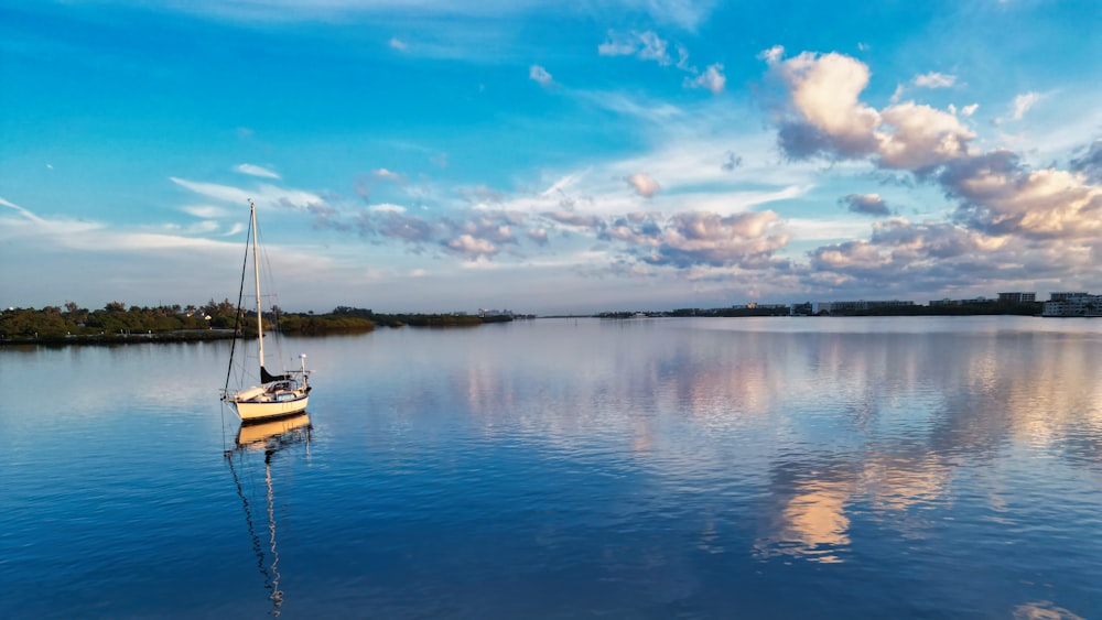 una barca a vela che galleggia su un lago sotto un cielo blu nuvoloso