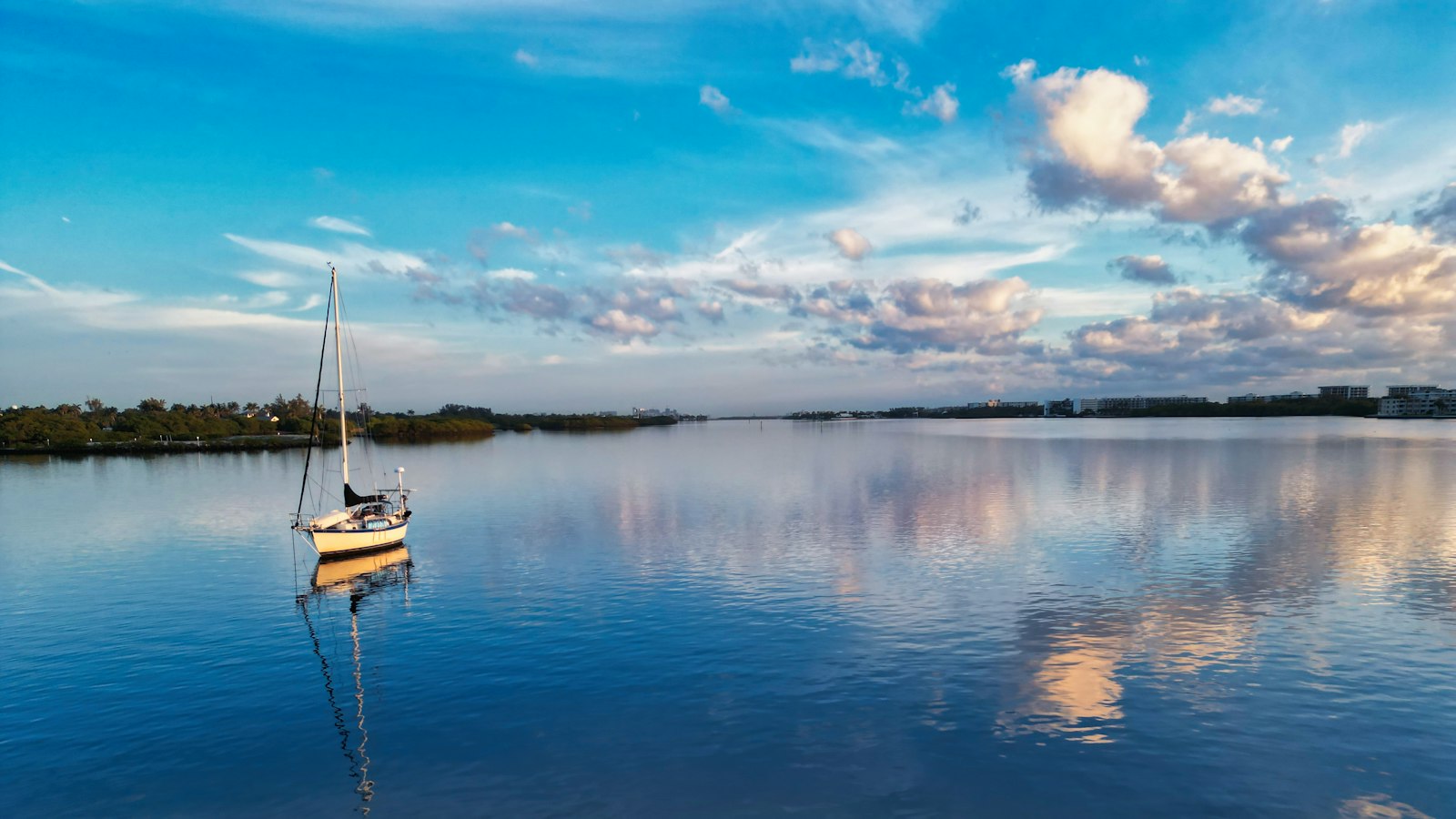 A sailboat floating on a lake under a cloudy blue sky.